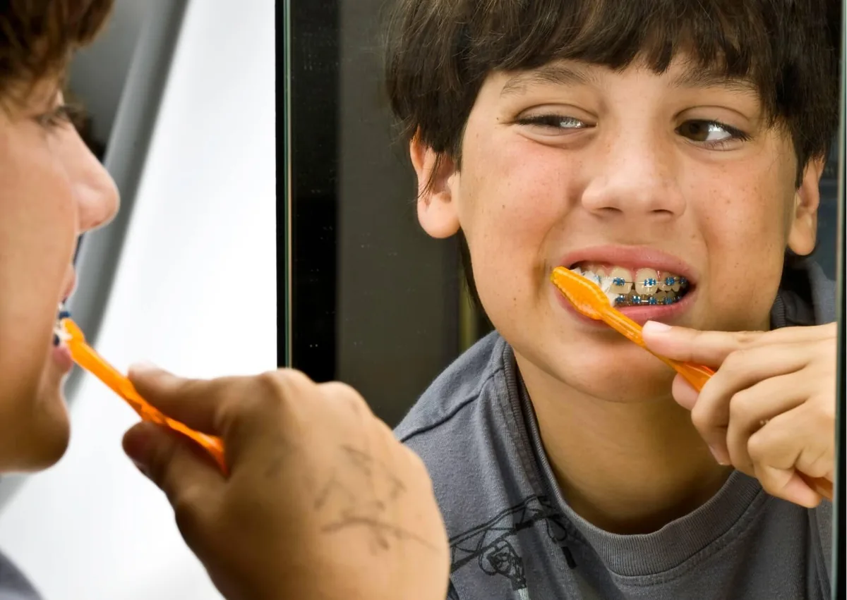 Child brushing teeth while wearing braces to maintain good oral hygiene.
